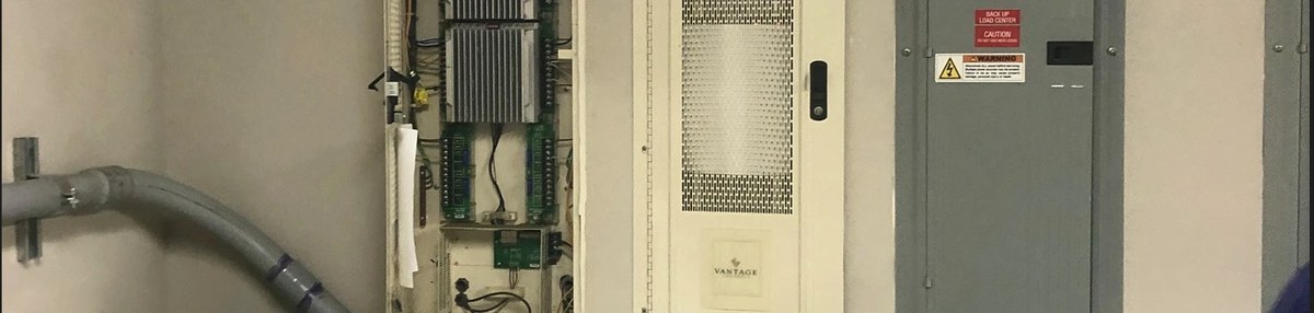 A lighting controls cabinet with control modules, beside a panel on a utility wall