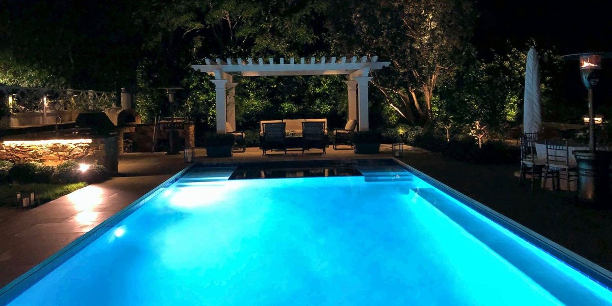 A lit pool and pergola at night, with the lighting system we installed