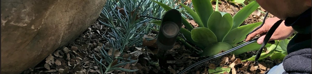 A technician repairing the wire at a spotlight fixture in a planting bed